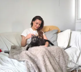 Fanny, sitting on a sofa, strokes a tortoiseshell cat lying on a blanket.